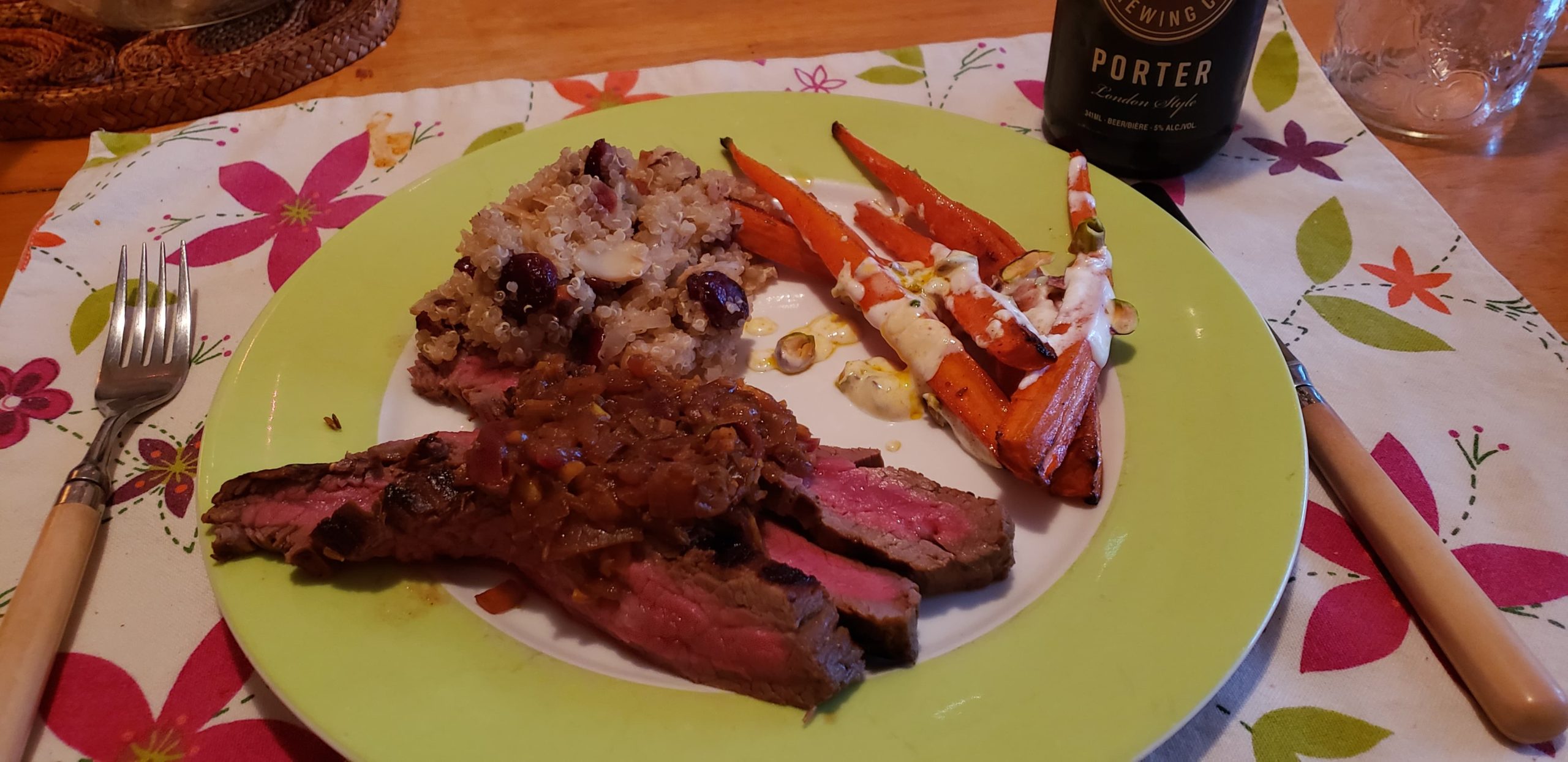 Plate showing a serving of flank steak, spiced roasted carrots, and quinoa pilaf with cranberries and almonds on a cheery spring placemat